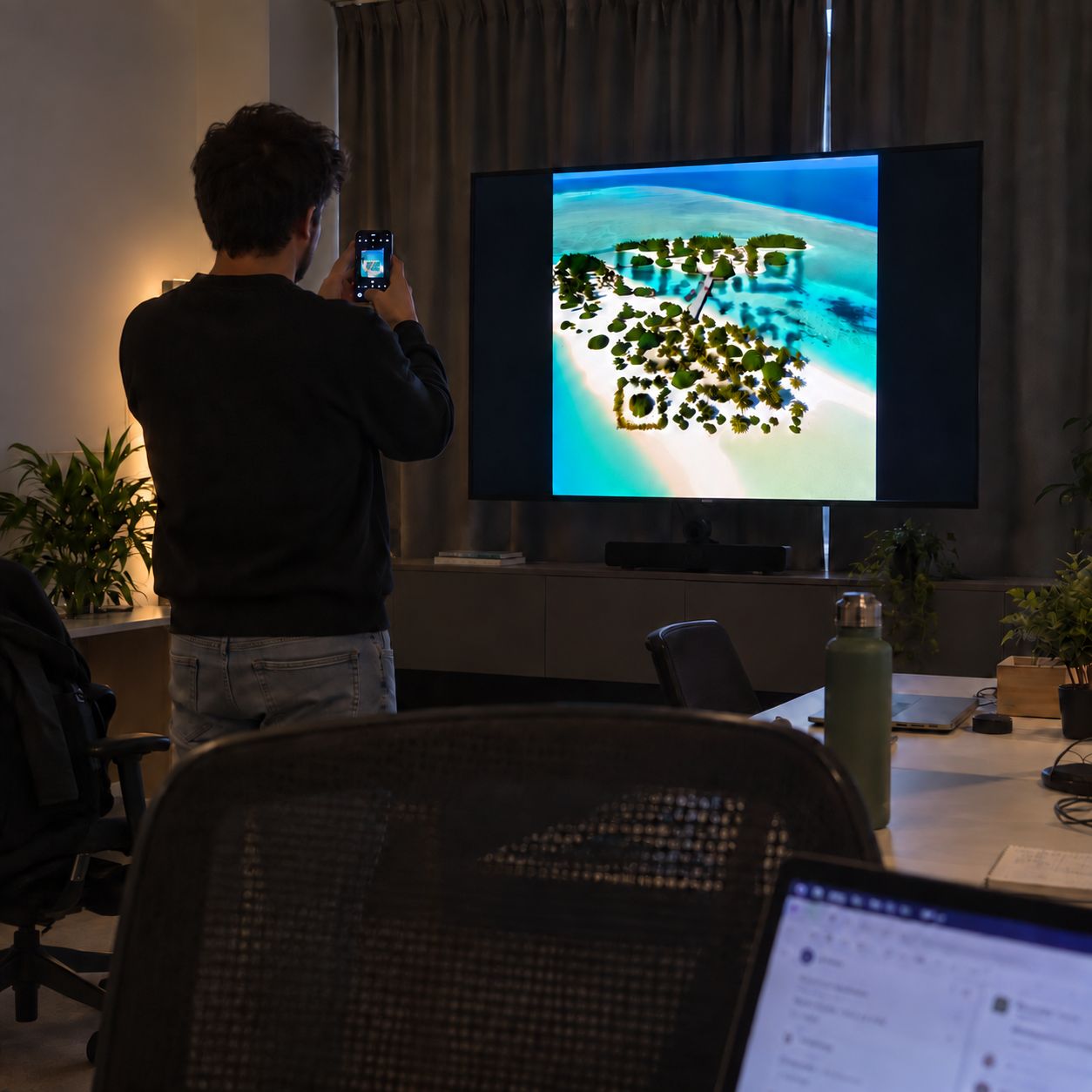 A team member stands well back from a large display in a darkened office, scanning a tropical-island StoryCode from several metres away with a phone camera.